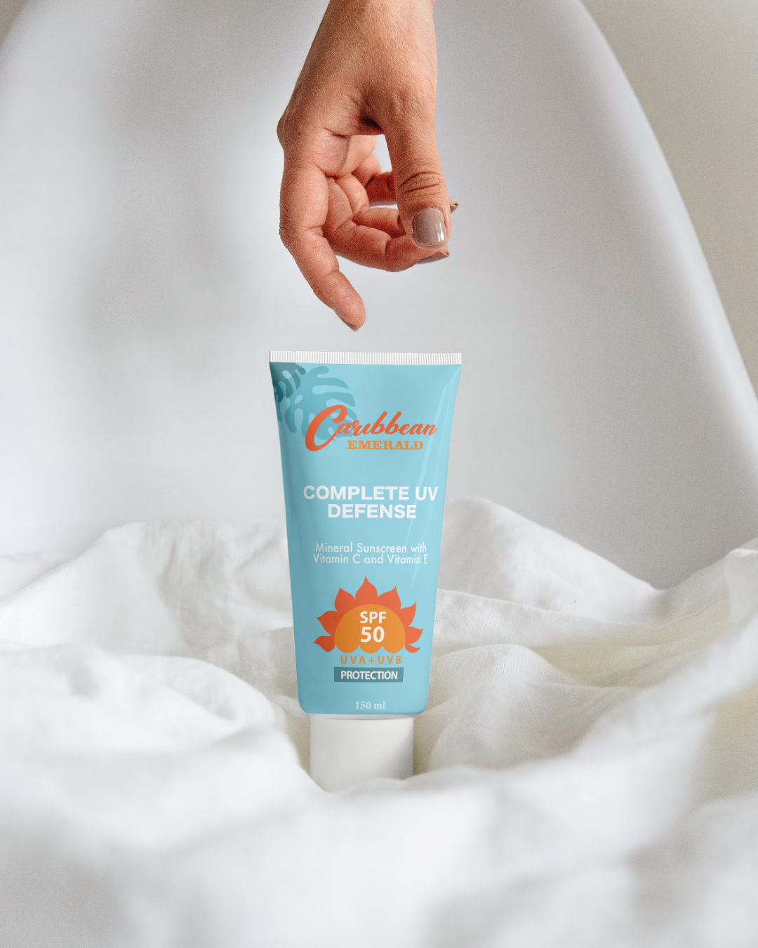 Hand holding a tube of Caribbean Emerald Mineral Reef-Safe Sun Complete UV Defense sunscreen on white fabric background